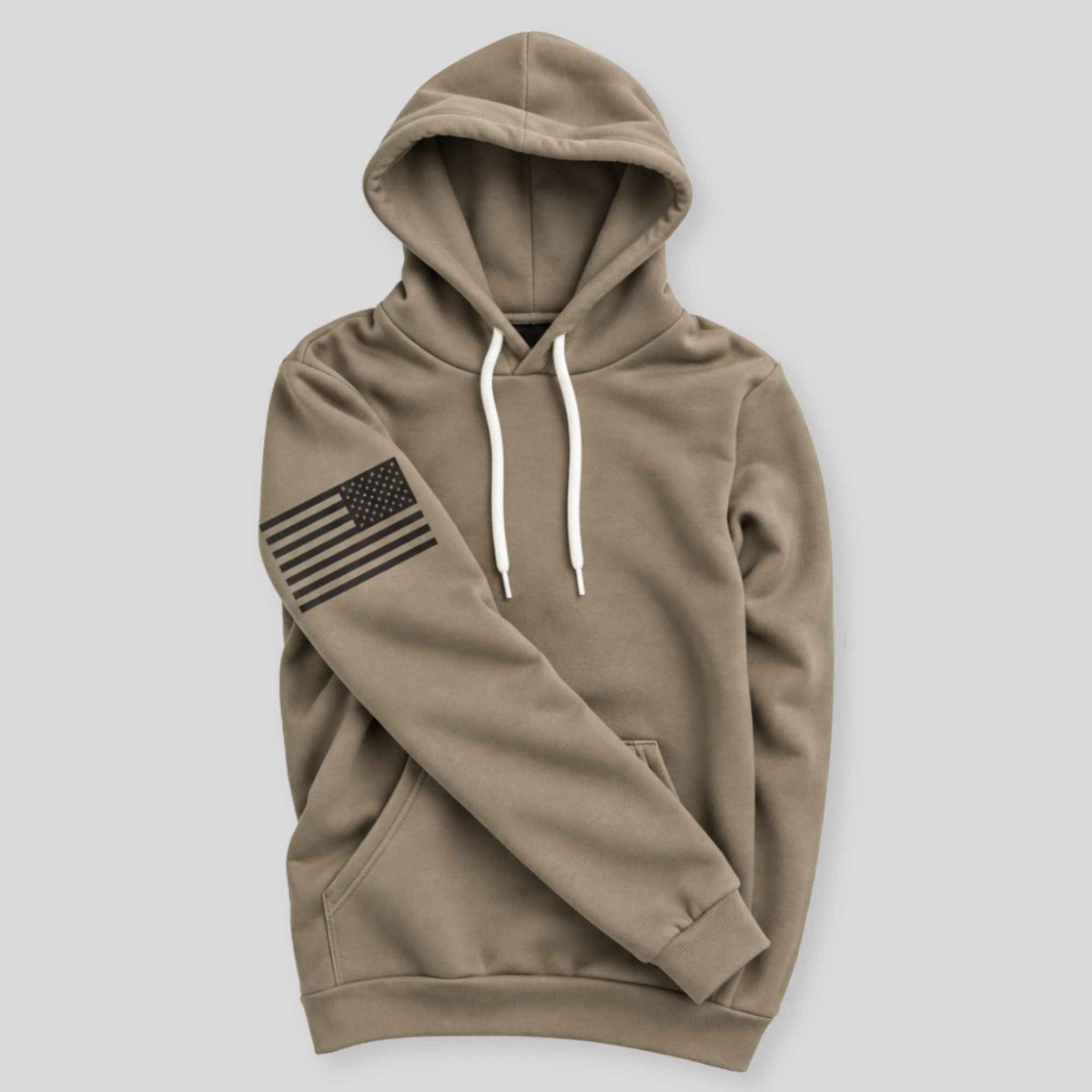 A khaki brown pullover hoodie with white drawstrings and a black distressed American flag graphic on the left sleeve, displayed on a neutral light gray background.