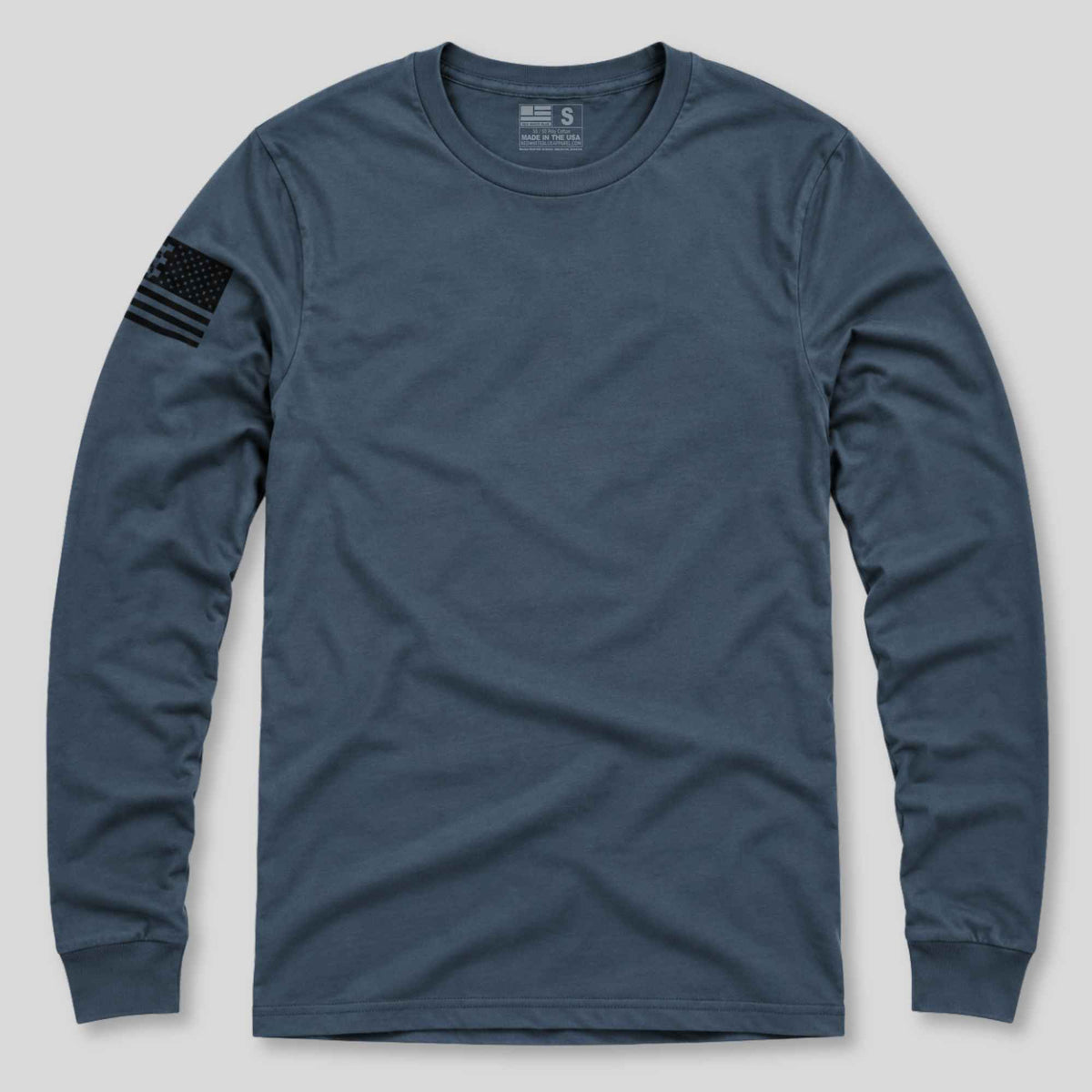 A navy blue long-sleeve crewneck t-shirt with a black distressed American flag patch on the right sleeve, displayed flat against a light gray background.