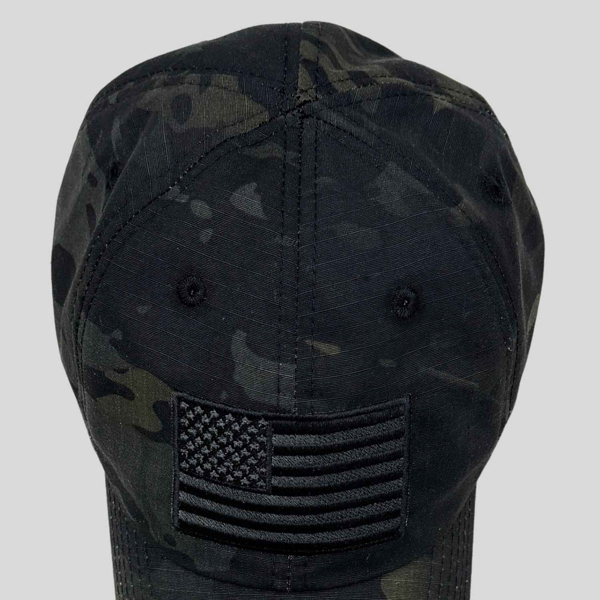 A black camouflage baseball cap featuring an embroidered black American flag patch on the front, shown against a solid light gray background.